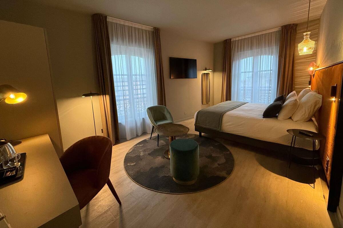 Ein Hotelzimmer mit Bett, Schreibtisch, Stuhl, rundem Tisch und Fernseher an der Wand.