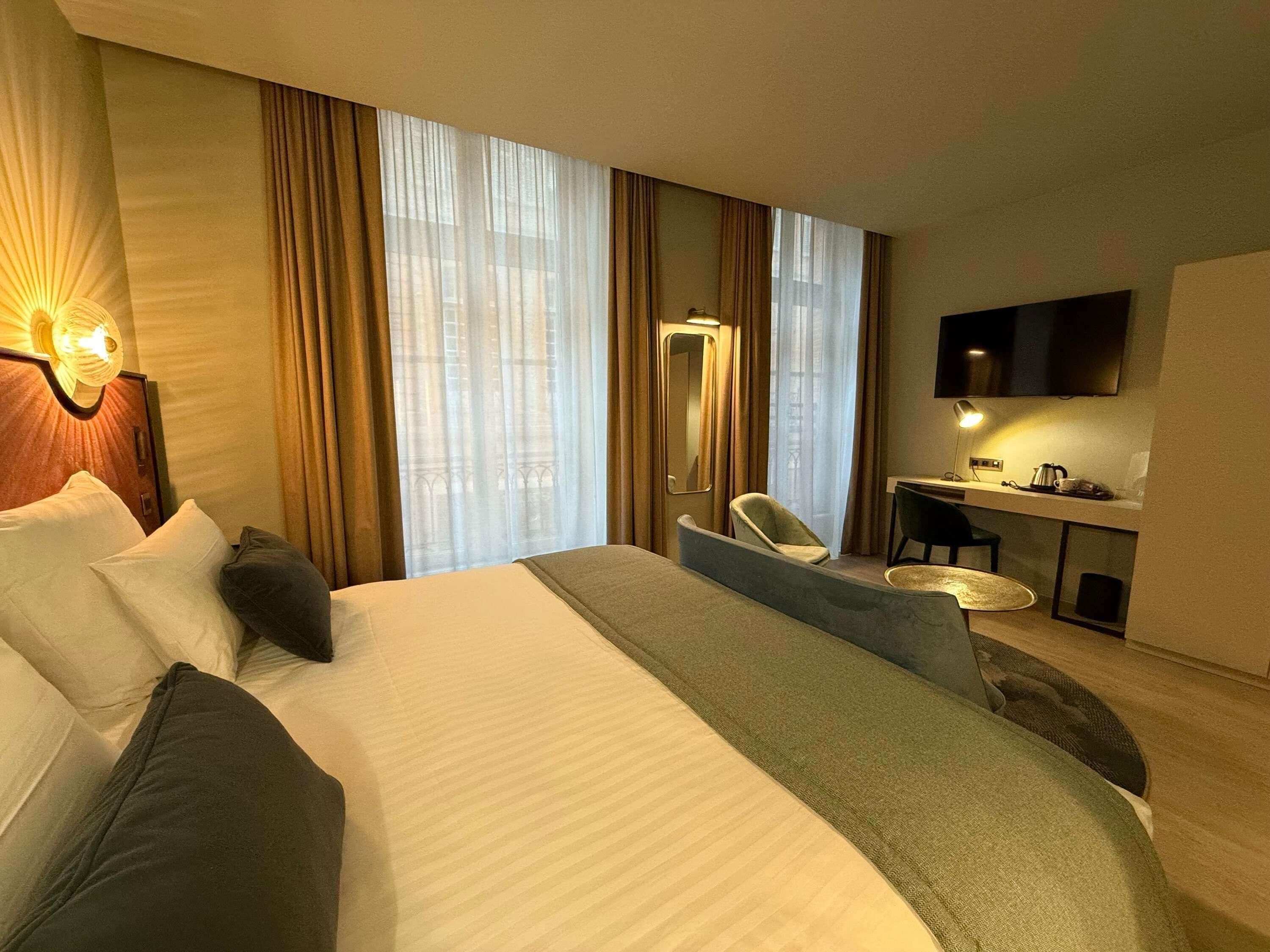 Une chambre d’hôtel avec un grand lit, un bureau, une chaise, une télévision et une fenêtre avec des rideaux.