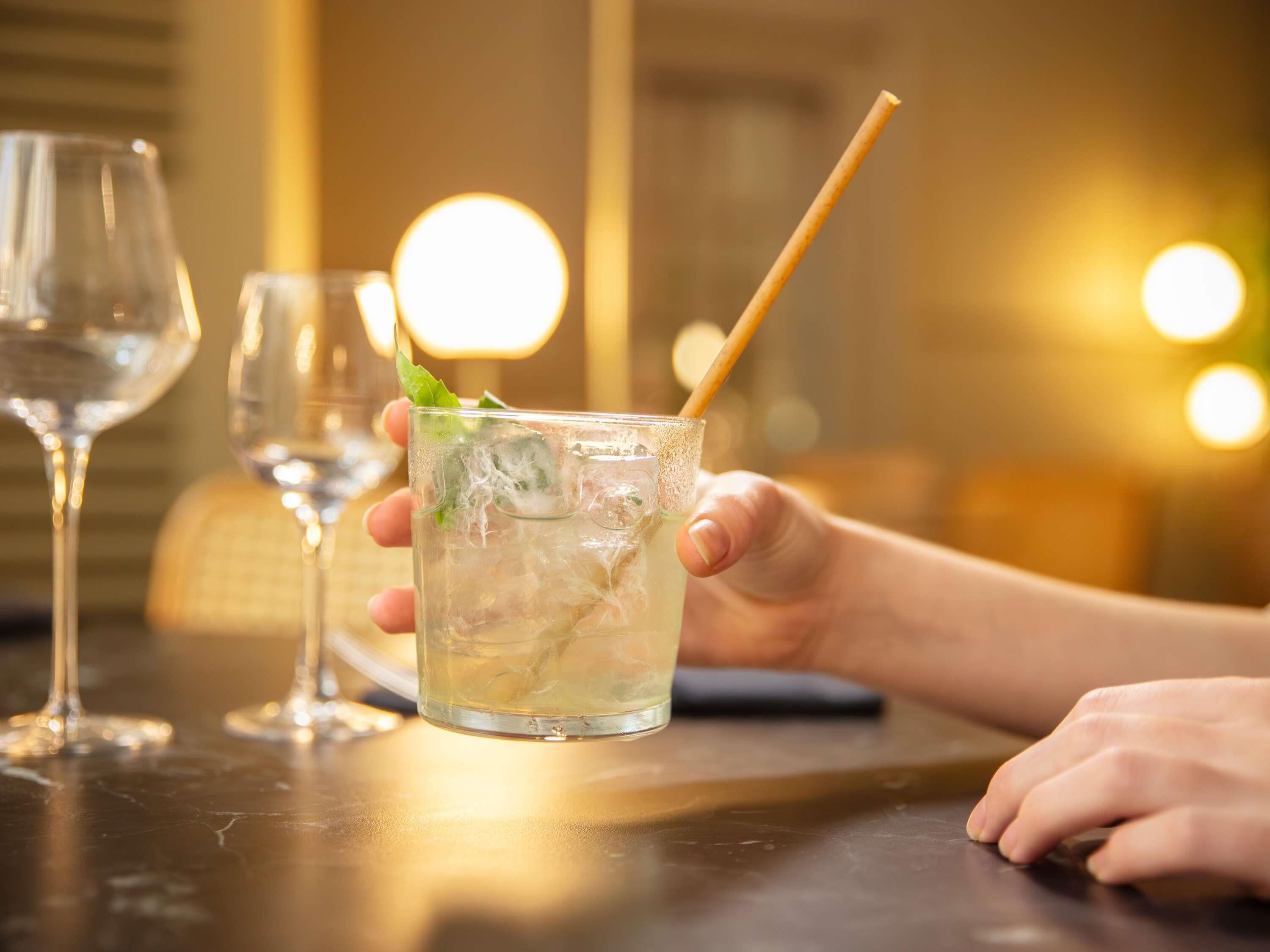 A glass of iced beverage with a straw and mint garnish, held by a person.