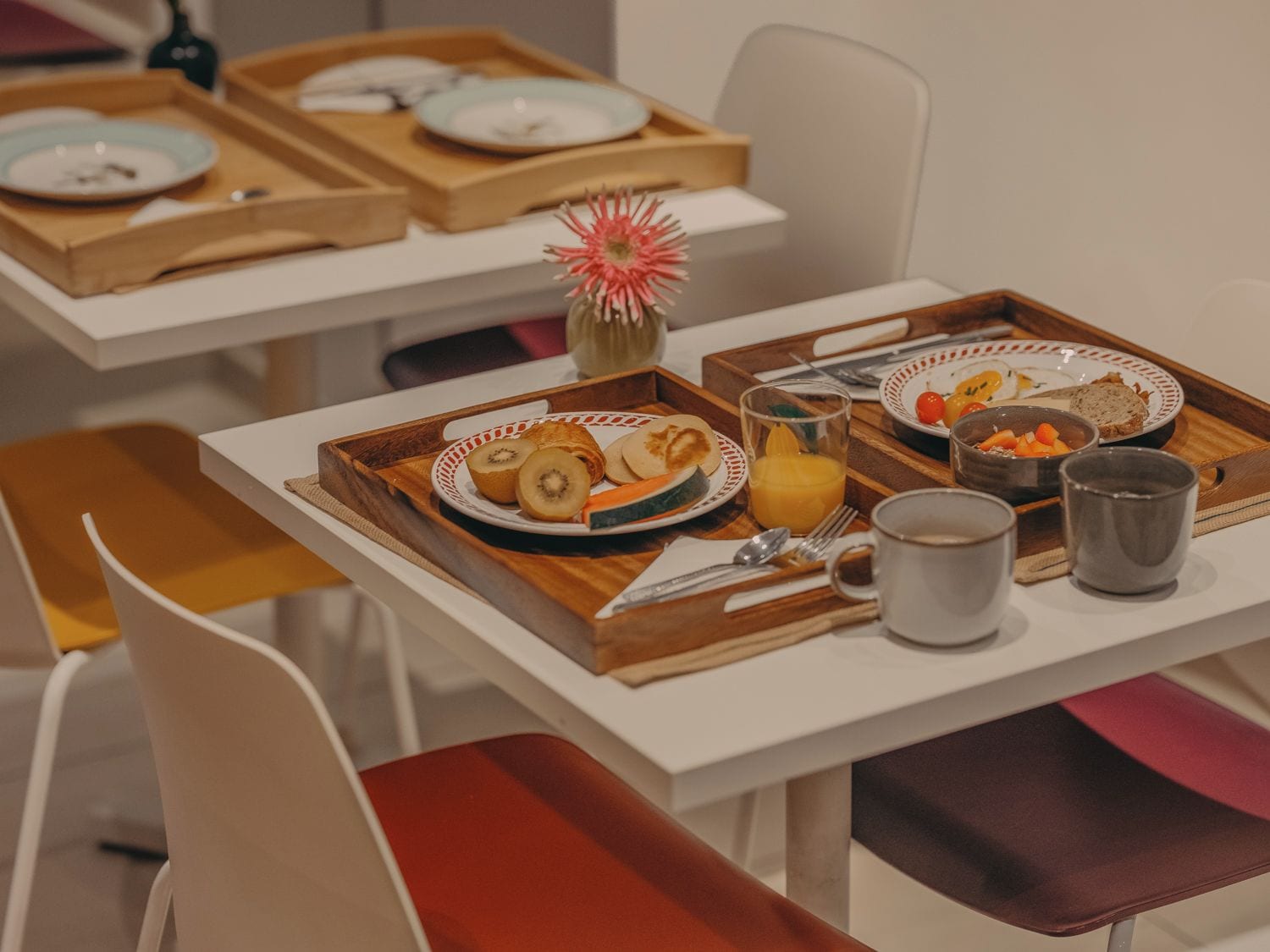 Desayuno con una bandeja que contiene tostadas, fruta y un vaso de jugo de naranja sobre una mesa blanca.