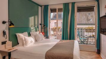 Habitación de hotel con cama, mesita de noche, lámpara, ventana con cortinas y vista al balcón exterior.