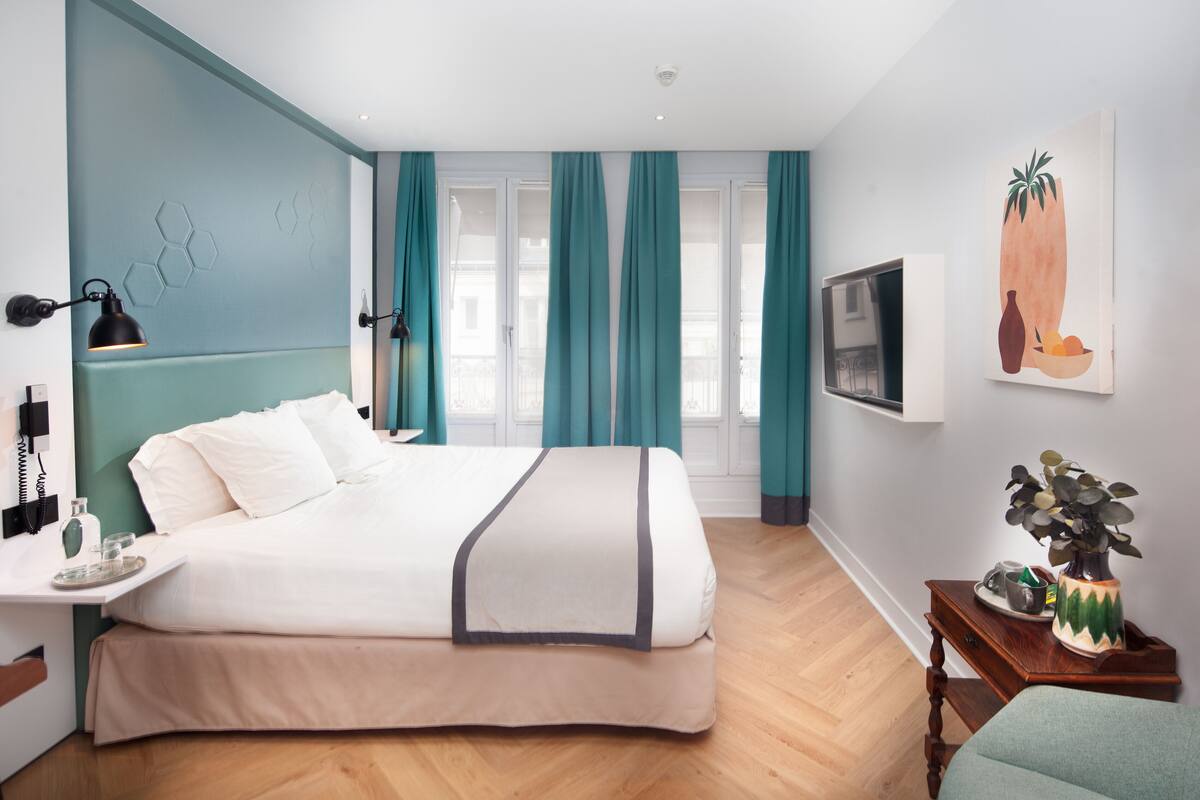 A modern bedroom with a large bed, teal curtains, a TV, and a painting on the wall.