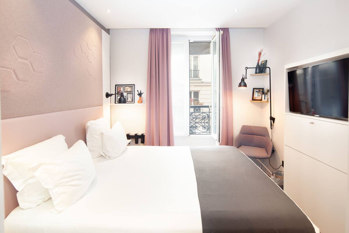 A hotel room with a bed, a desk, a chair, a TV, and a balcony view.