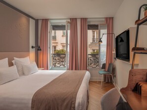 A hotel room with a bed, a desk, a chair, a TV, and a balcony with curtains. - Hôtel Vendome Saint Germain (Paris)