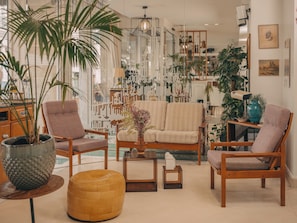 A modern living room with a sofa, chairs, and a coffee table. There are plants and decorative items on shelves. - Hôtel Vendome Saint Germain (Paris)