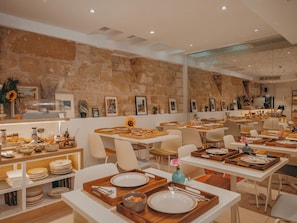 A restaurant with multiple tables set for dining, a stone wall, and various dining accessories. - Hôtel Vendome Saint Germain (Paris)