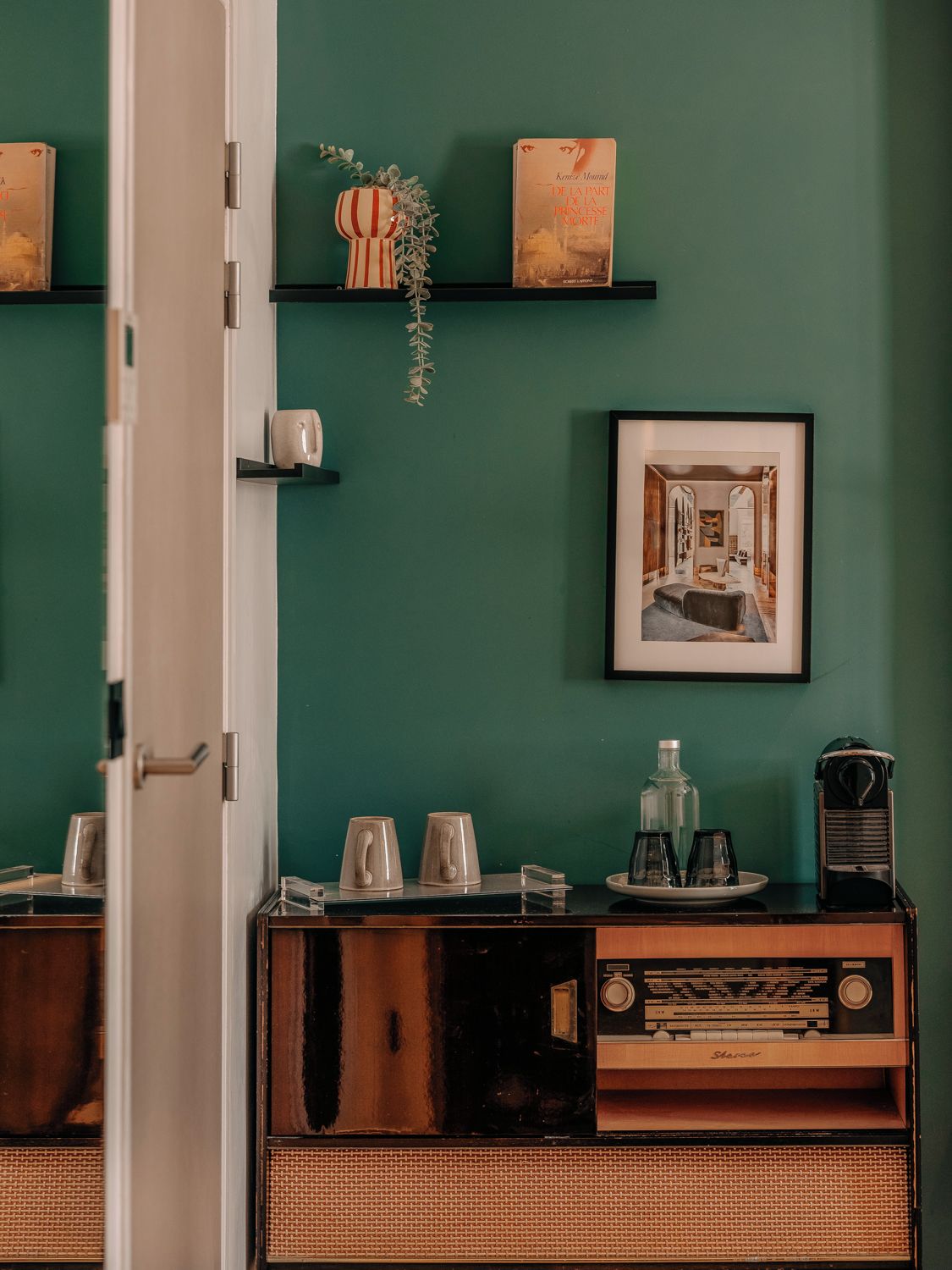 Una habitación con pared verde, un cuadro enmarcado, una estantería con libros y una radio antigua.