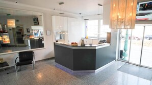 A modern reception area with a central counter, a seating area, and a large window providing natural light. - Hotel Am Zoo (Frankfurt)