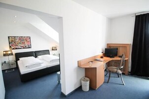 A hotel room with a bed, desk, chair, and a painting on the wall.