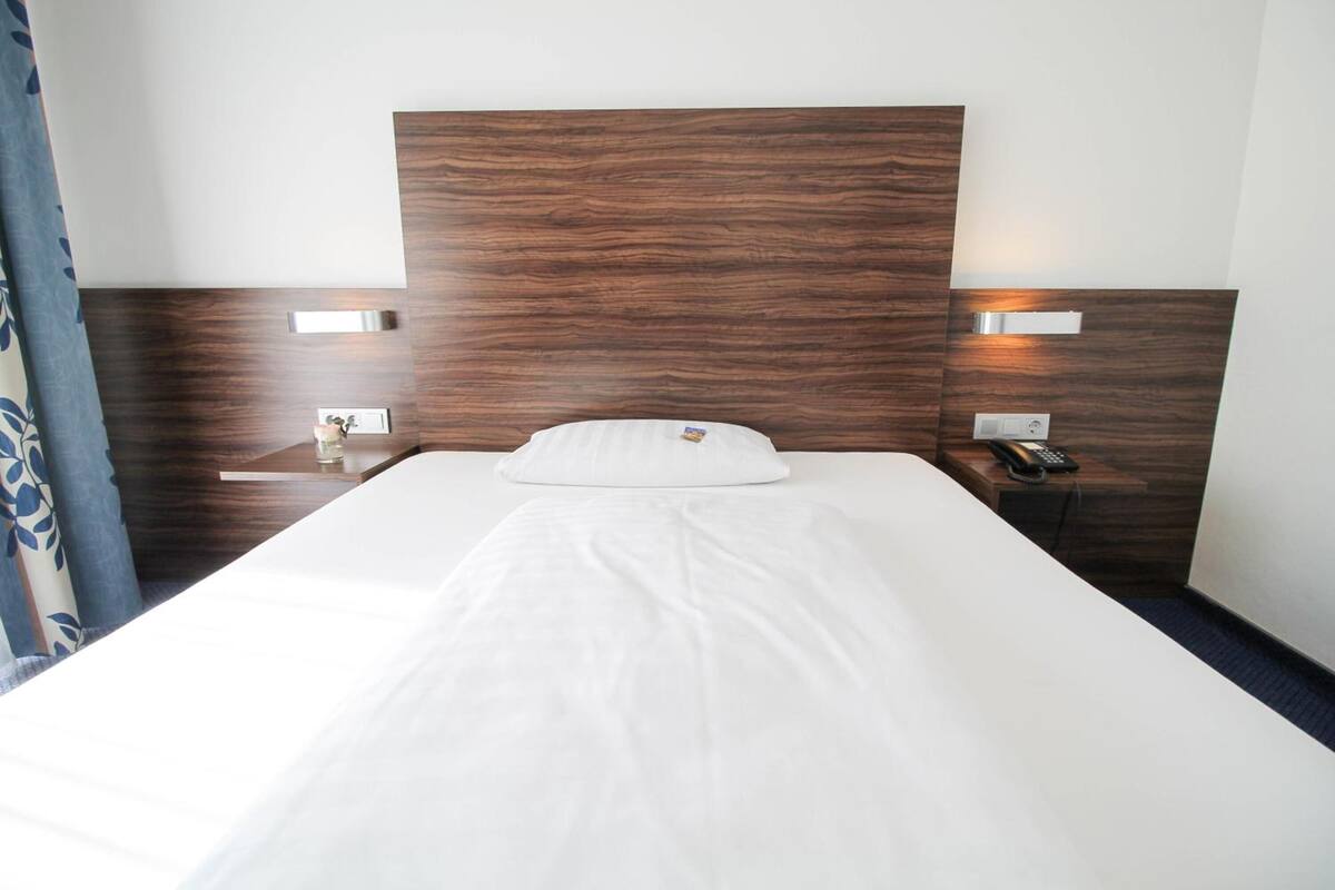 Una habitación de hotel con una cama grande, cabecera de madera, mesitas de noche con lámparas y un teléfono.