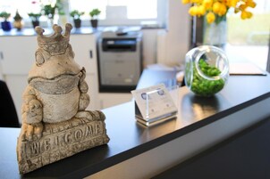 Una reception con una scultura di rana in pietra, un vaso di vetro con piante verdi e una stampante sullo sfondo.