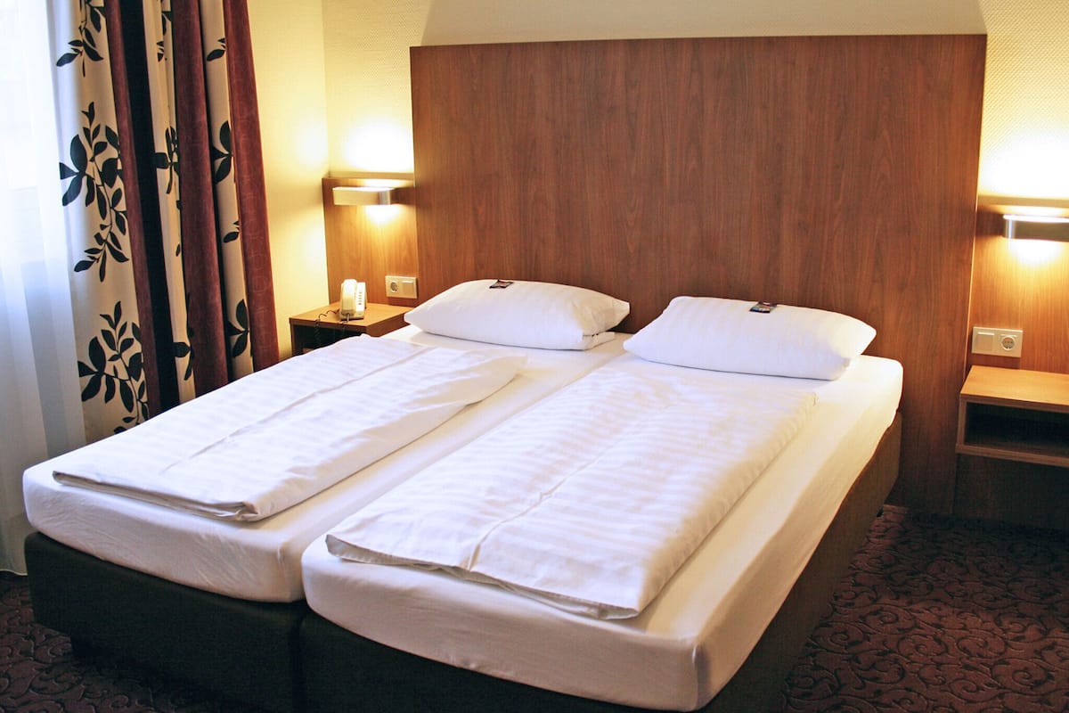 Una cama doble con dos almohadas, cabecera de madera, lámparas de noche y alfombra estampada.