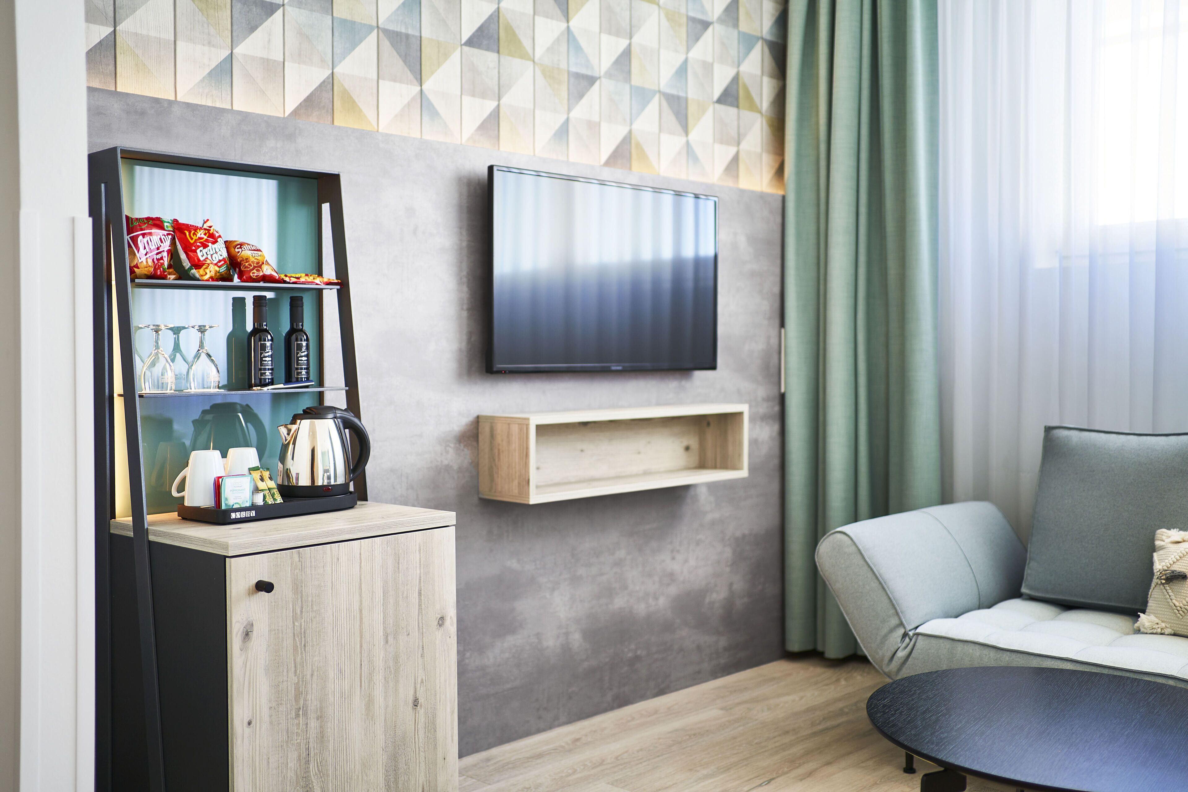 Ein modernes Wohnzimmer mit einer Couch, einem flachbildfernseher an der Wand, einer Holzkommode mit Snacks und Getränken und einem Couchtisch.
