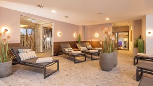 A spa area with multiple lounge chairs, large potted plants, and a well-lit interior.