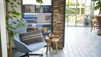 Ein moderner Lounge-Bereich mit einem blauen Sessel, einem kleinen Holztisch mit Teekanne sowie einem Bücherregal mit Zeitschriften und Büchern.