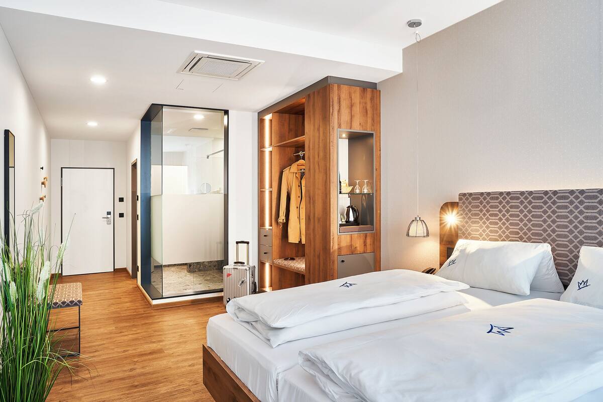 A modern hotel room with a wooden wardrobe, a bed with white linens, and a glass shower enclosure.