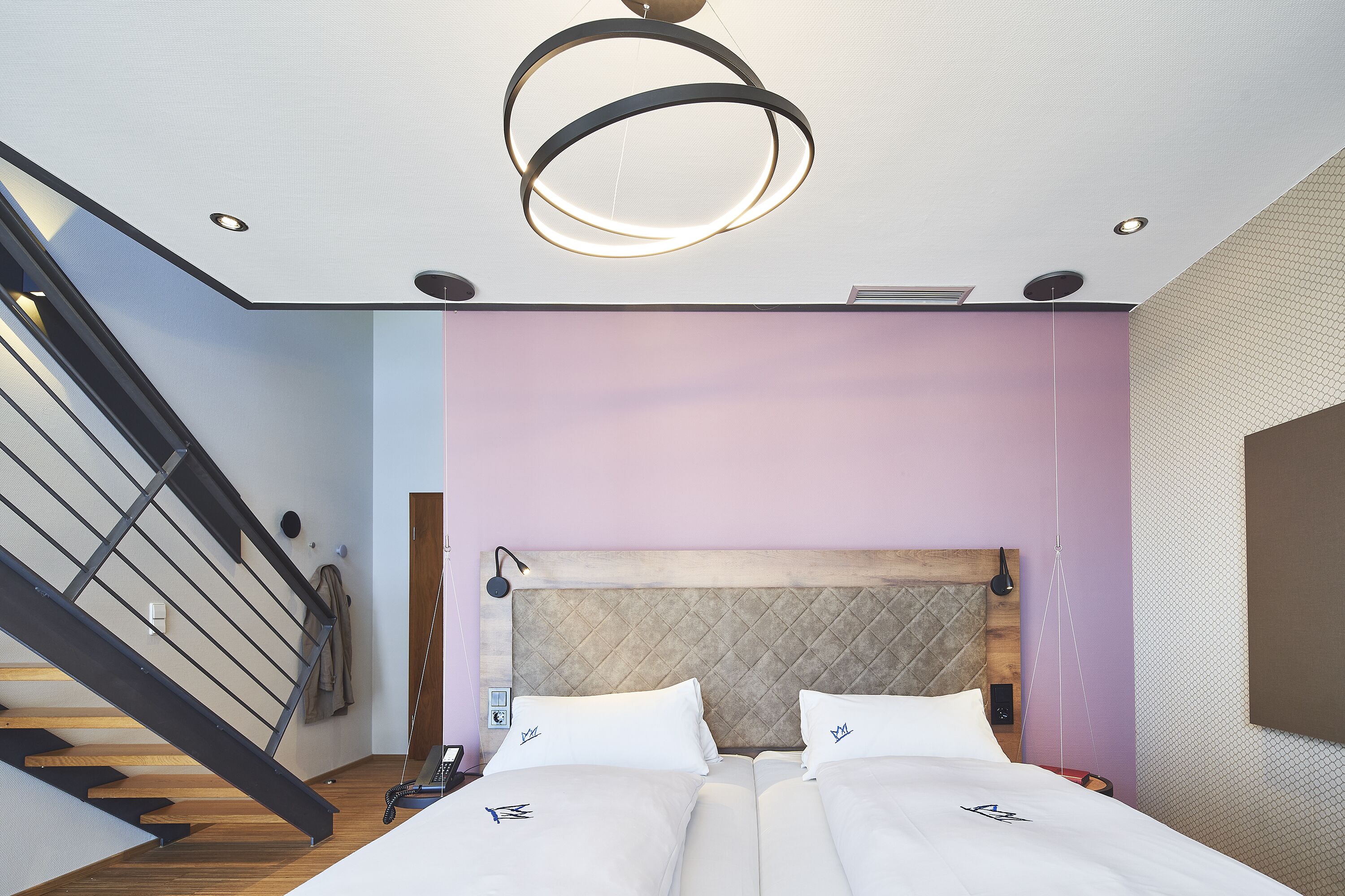 A modern bedroom with a bed, a headboard, a staircase, and a pendant light.