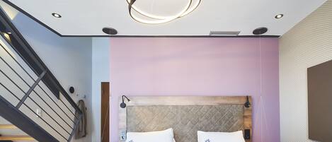 A modern bedroom with a bed, a headboard, a staircase, and a pendant light.