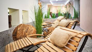 A spa area with wooden loungers, a large rock, and tall grasses.