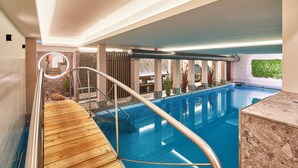 An indoor swimming pool with a wooden deck, a glass balustrade, and a stone wall.