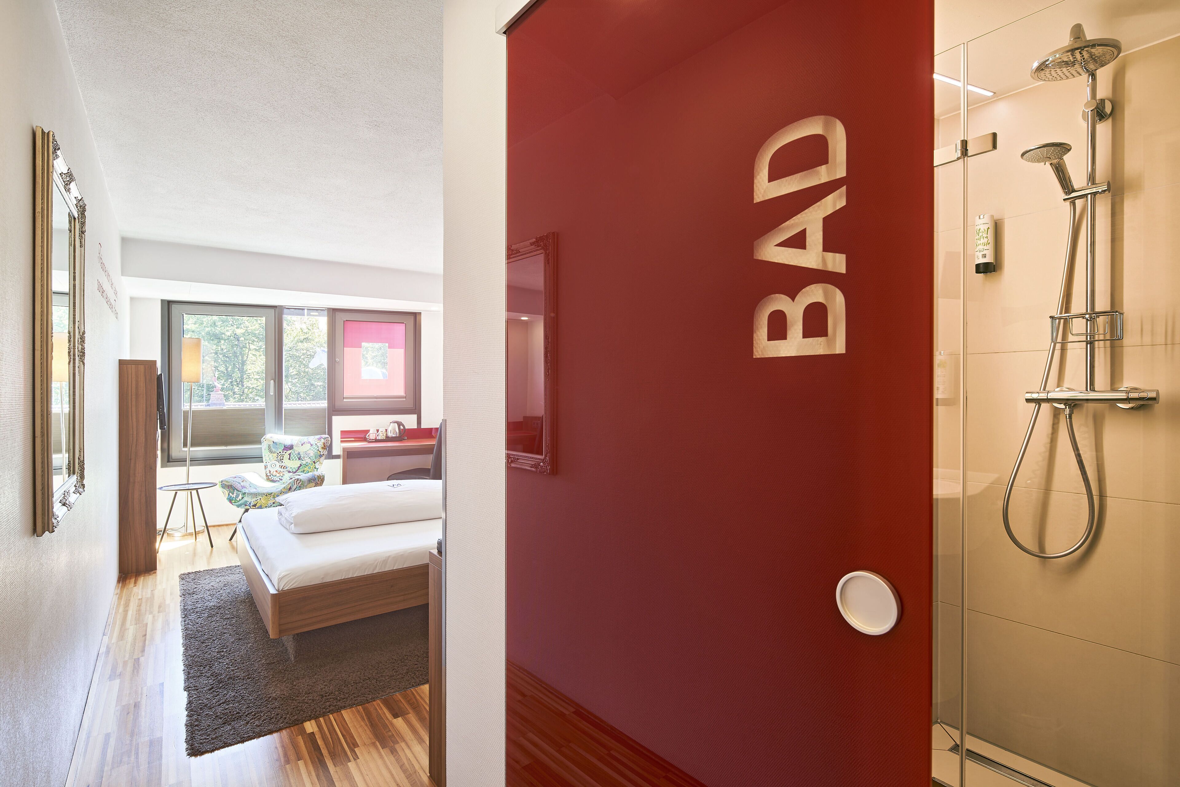 A modern hotel room with a large bed, a sitting area, and a bathroom with a shower.