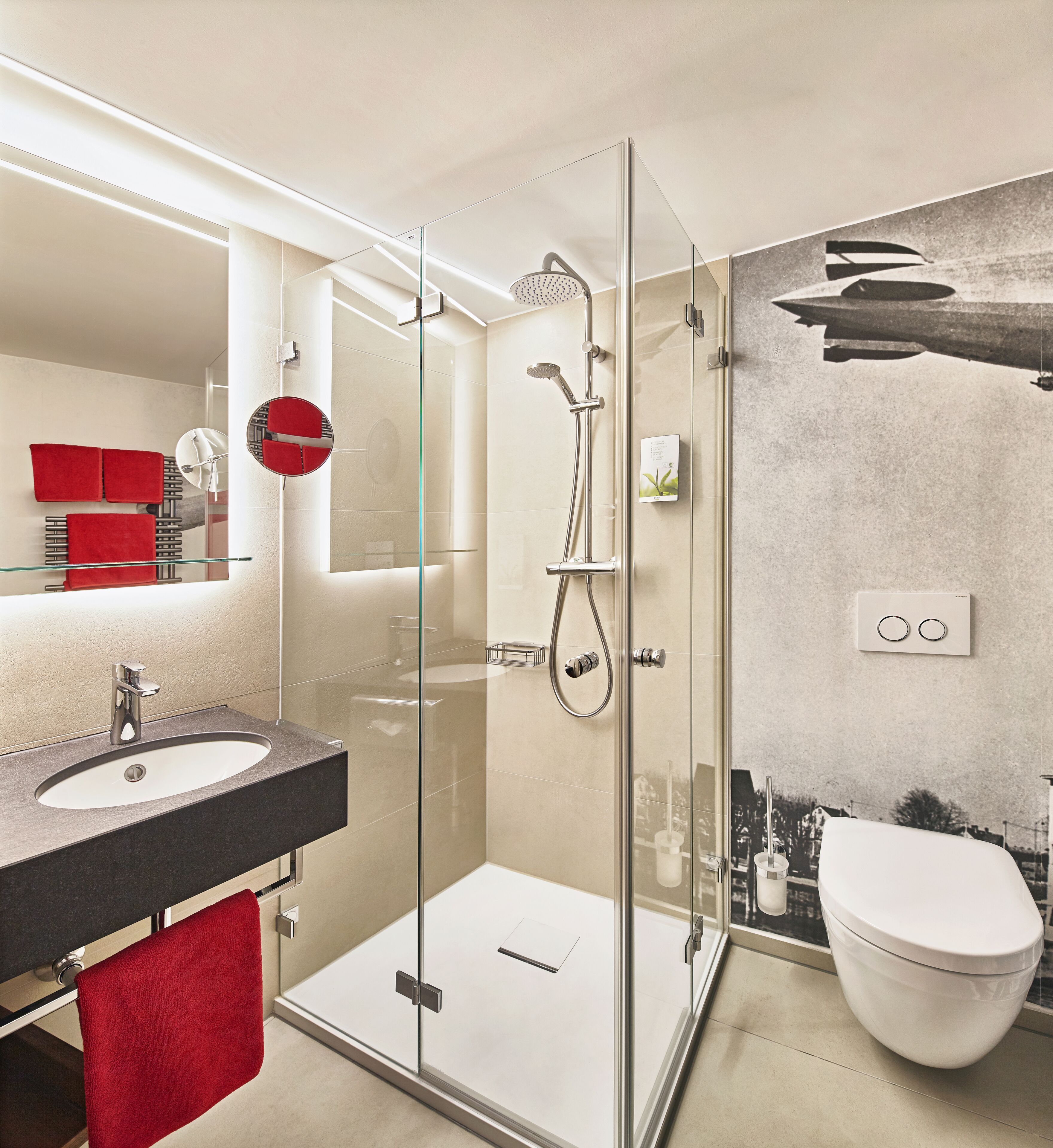 Une salle de bain moderne avec une douche à parois de verre, un lavabo surmonté d’une serviette rouge et des toilettes.