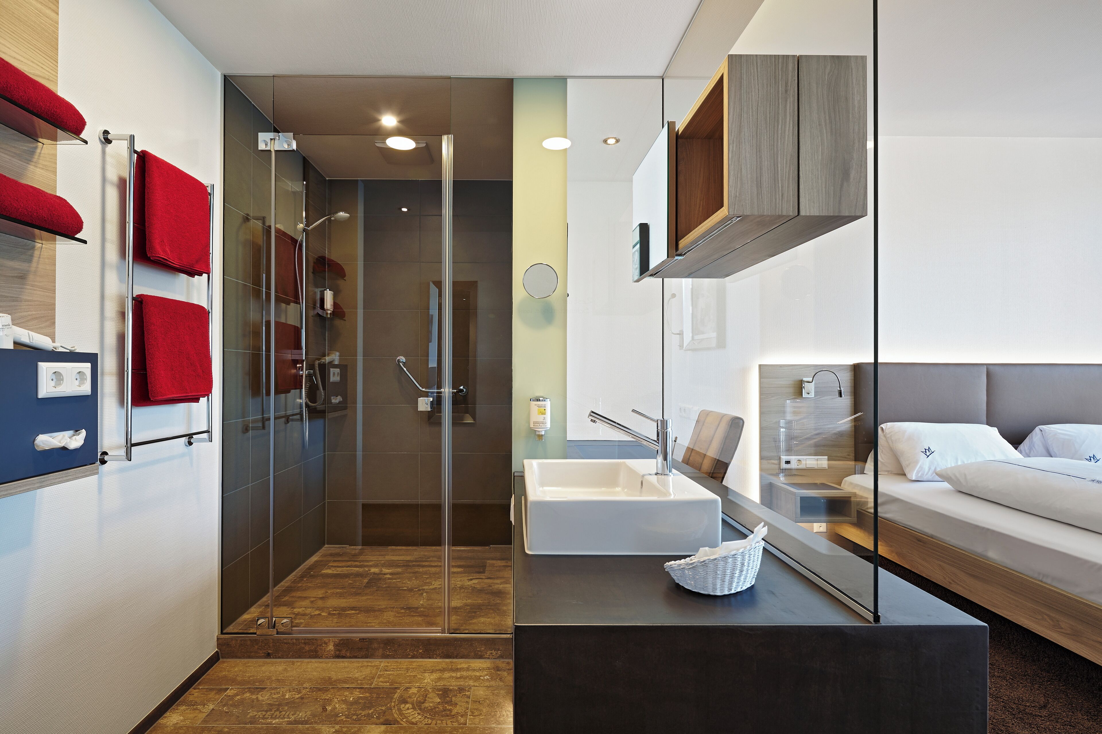 Un baño moderno con cabina de ducha de vidrio, un lavamanos blanco y una mesita de noche con una cesta.