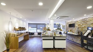 A modern hotel lobby with a wooden reception desk, a stone accent wall, and a large window providing natural light.