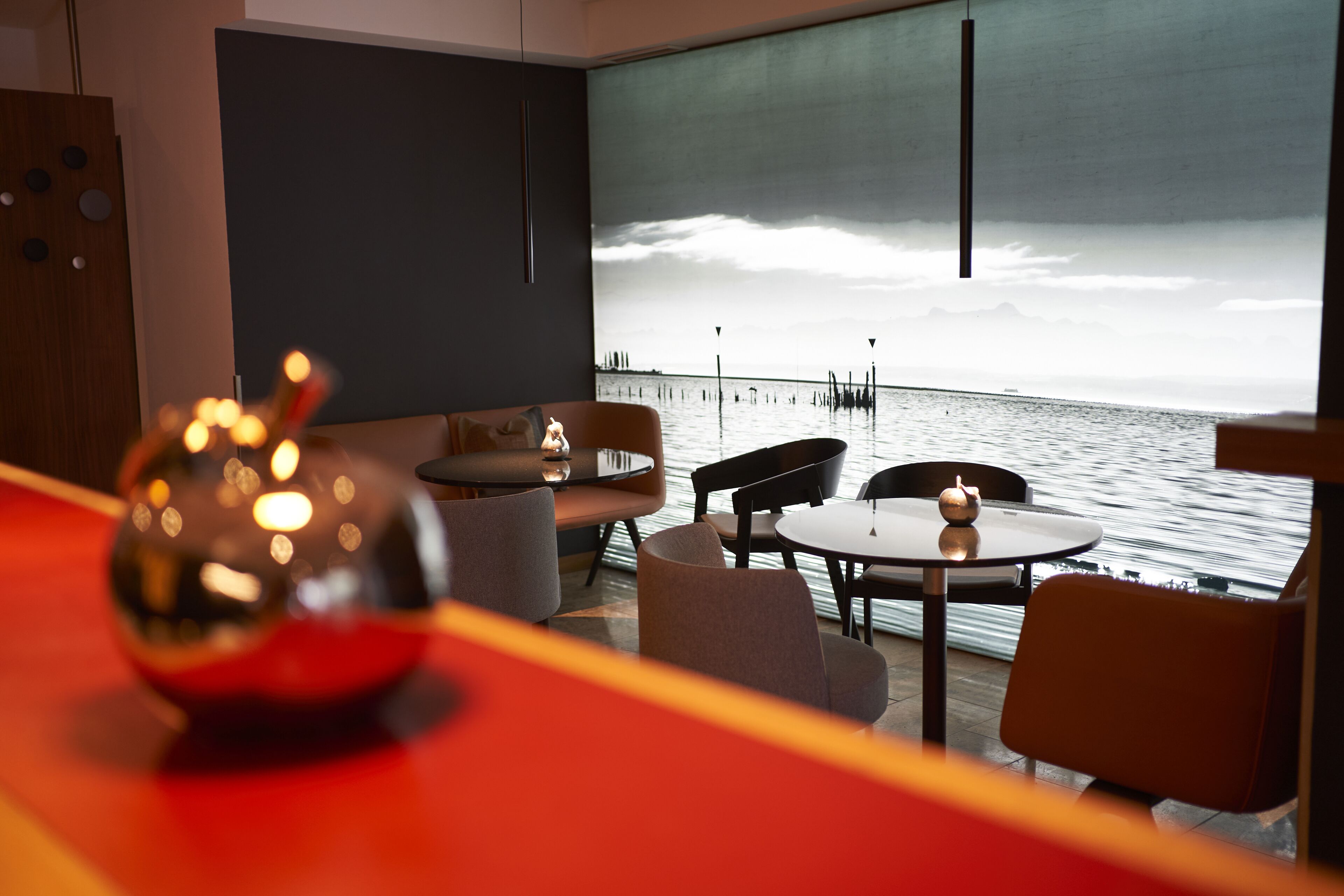 Een modern interieur met uitzicht op het water, met een ronde tafel, stoelen en een decoratieve glazen bol.