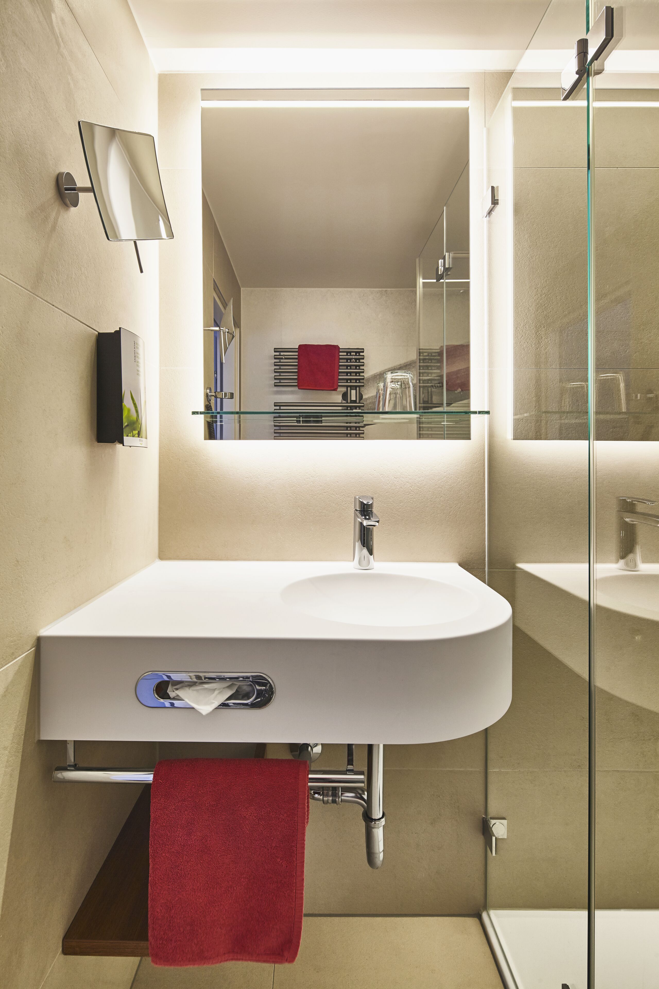 Un baño moderno con un lavabo blanco, cabina de ducha con paredes de vidrio y una toalla roja colgada en la pared.