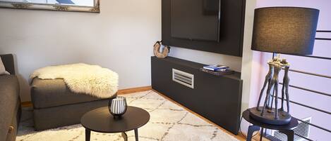 A modern living room with a sofa, a small round table, a lamp, a television, and a decorative item on a console table.
