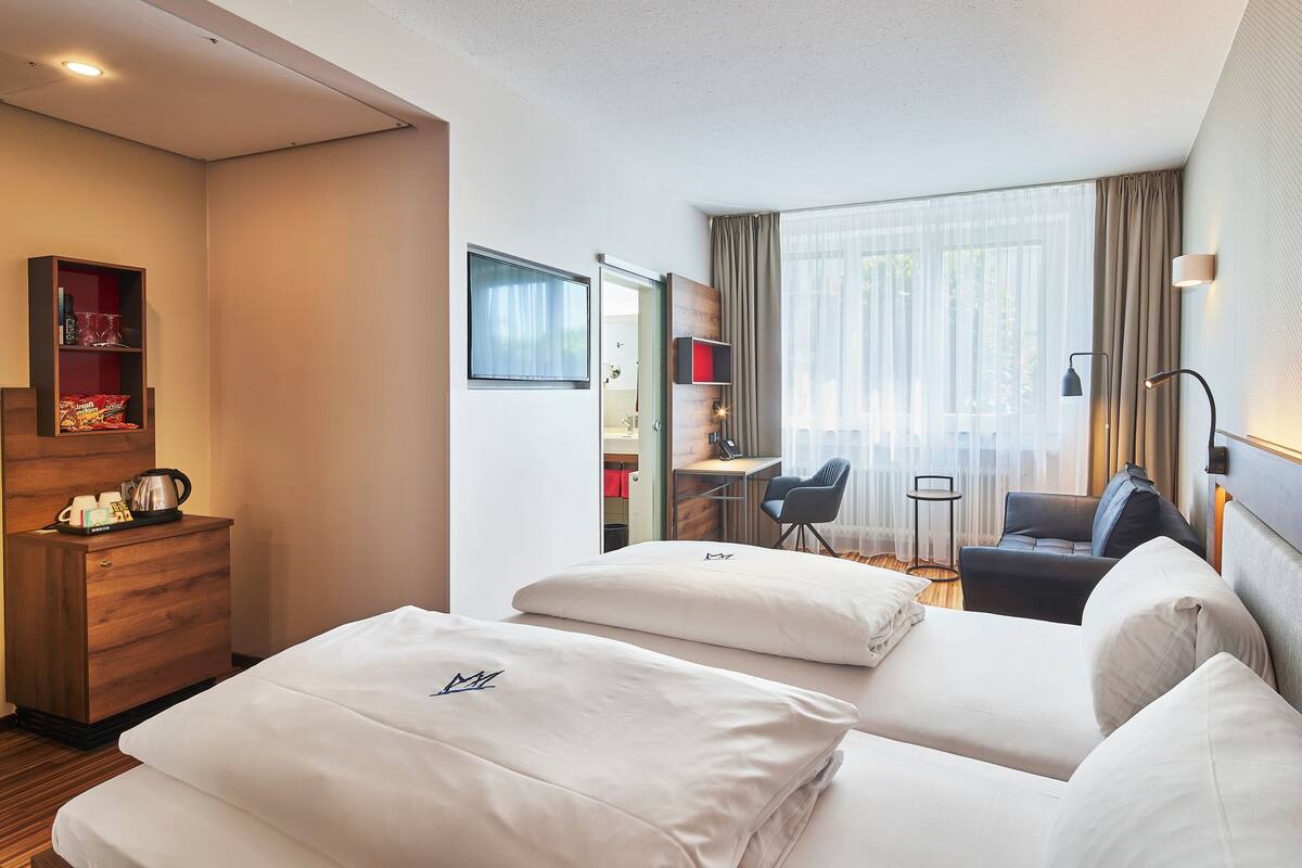 A hotel room with a bed, a desk, a chair, a small table, and a wardrobe.