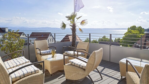 A balcony with wicker furniture, a flag, and a view of the sea.