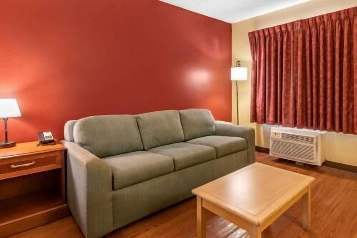 A room with a sofa, a wooden table, a lamp, a heater, and a window with curtains.
