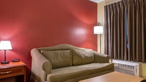 Et værelse med en grøn sofa, et træbord, et natbord med lampe og et vindue med gardiner.
