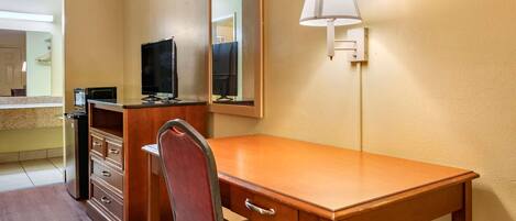 A hotel room with a wooden desk, a chair, a television, a mirror, and a lamp.