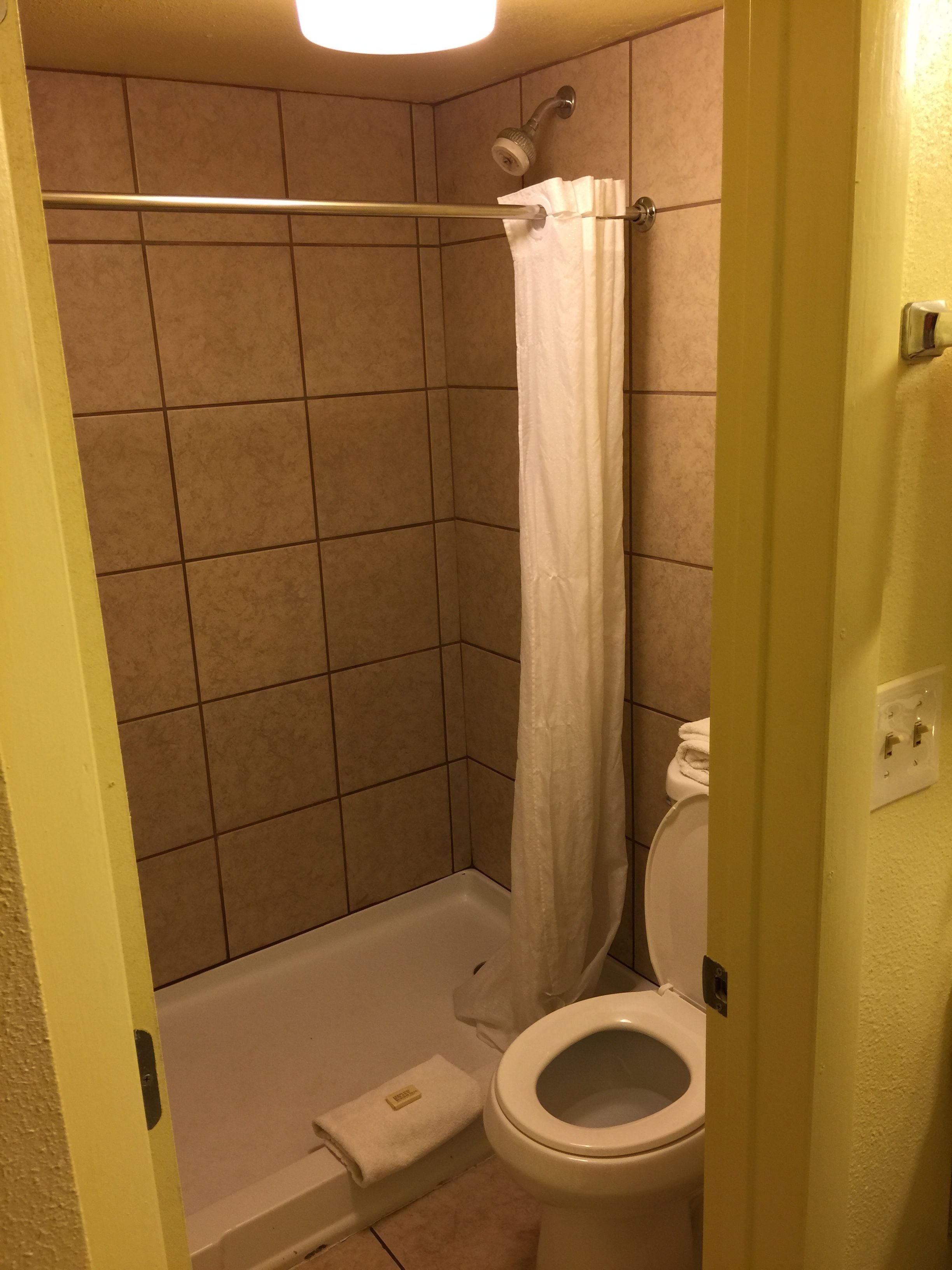 A small bathroom with a shower, toilet, and a towel on the floor.
