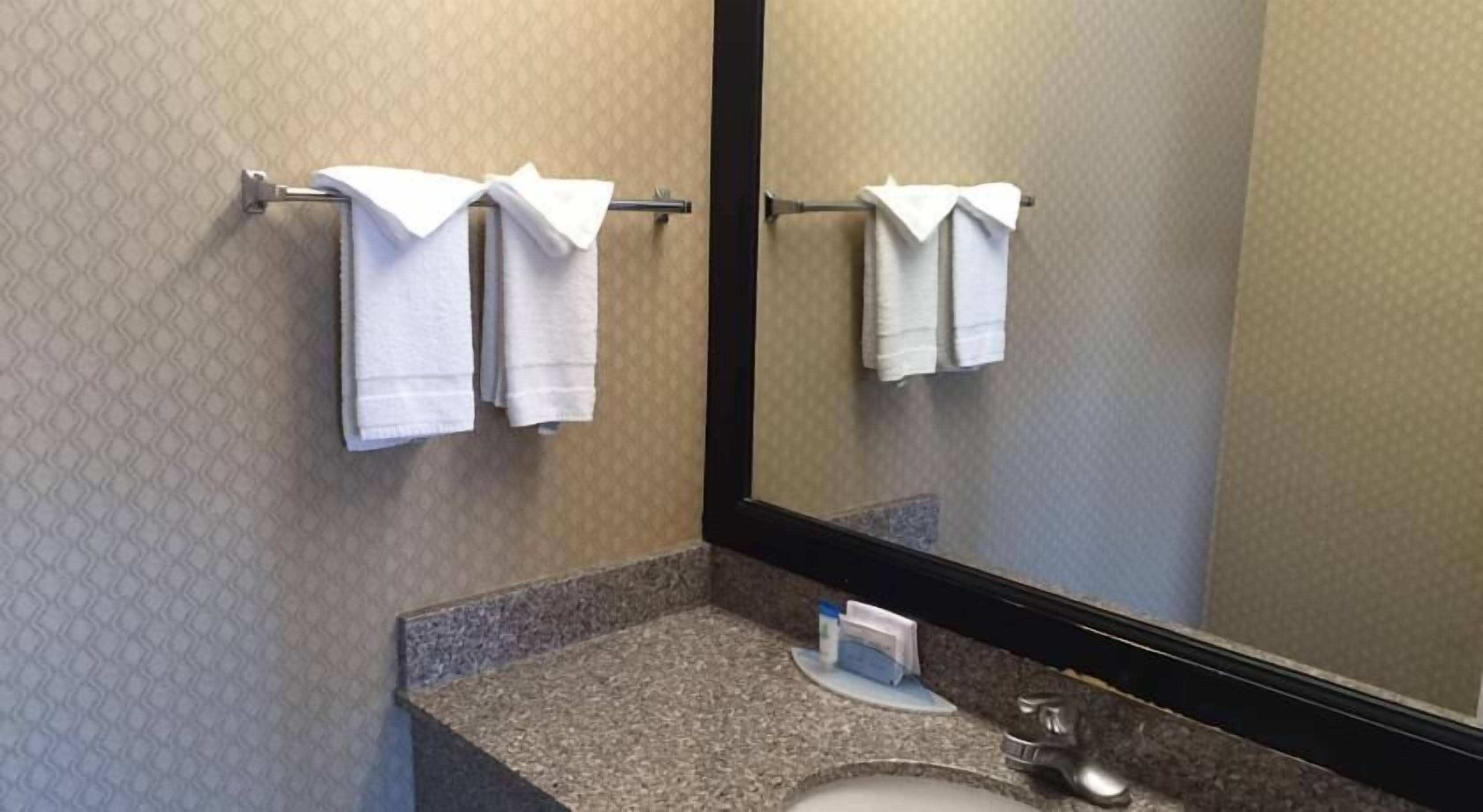 A bathroom with a granite countertop, a sink, and a mirror. There are two white towels hanging on a towel rack.
