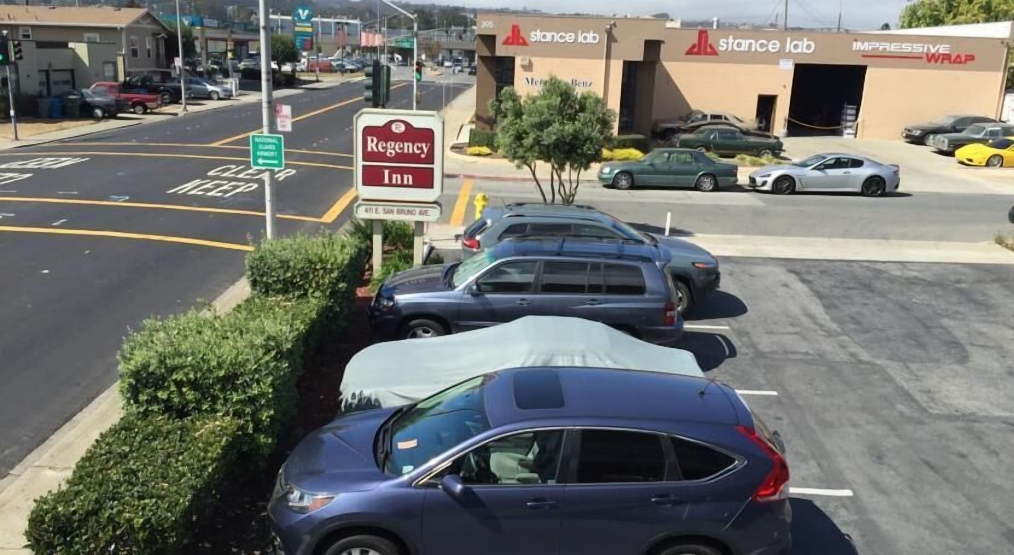 Un estacionamiento con varios autos, el cartel de Regency Inn y un edificio de Stance Lab al fondo.