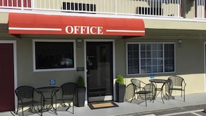 An office building with a red awning, a glass door entrance, and outdoor seating with chairs and tables. - Regency Inn SFO Airport (San Bruno)
