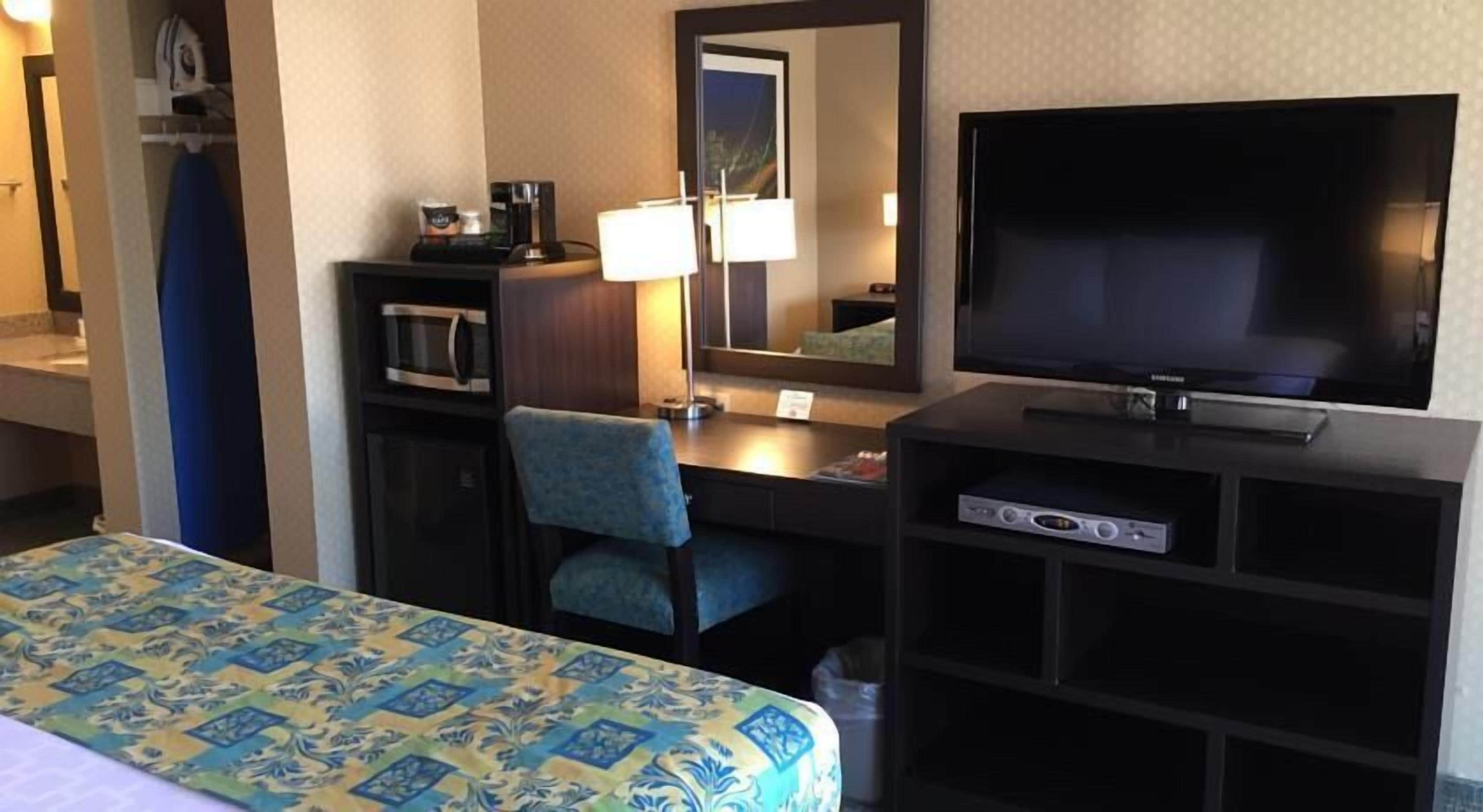 A hotel room with a bed, a desk with a television, a microwave, and a chair.