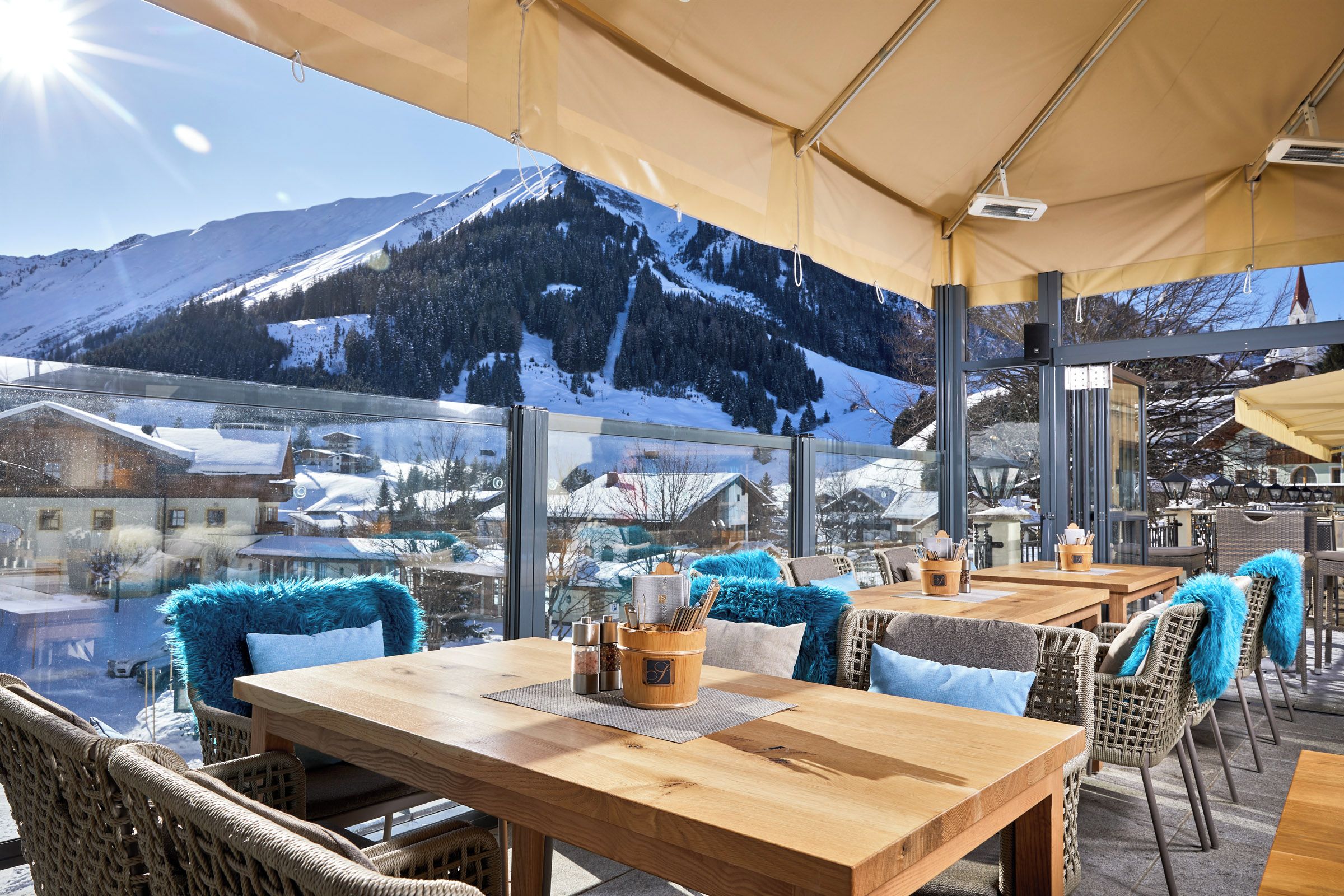 Ein Restaurant mit Außenbereich, großen Fenstern und Blick auf schneebedeckte Berge.