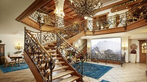 Una gran escalera con barandillas de metal ornamentadas y escalones de madera, que conduce a un balcón con vistas a la montaña.