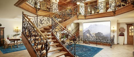 A grand staircase with ornate metal railings and wooden steps, leading to a balcony with a mountain view.