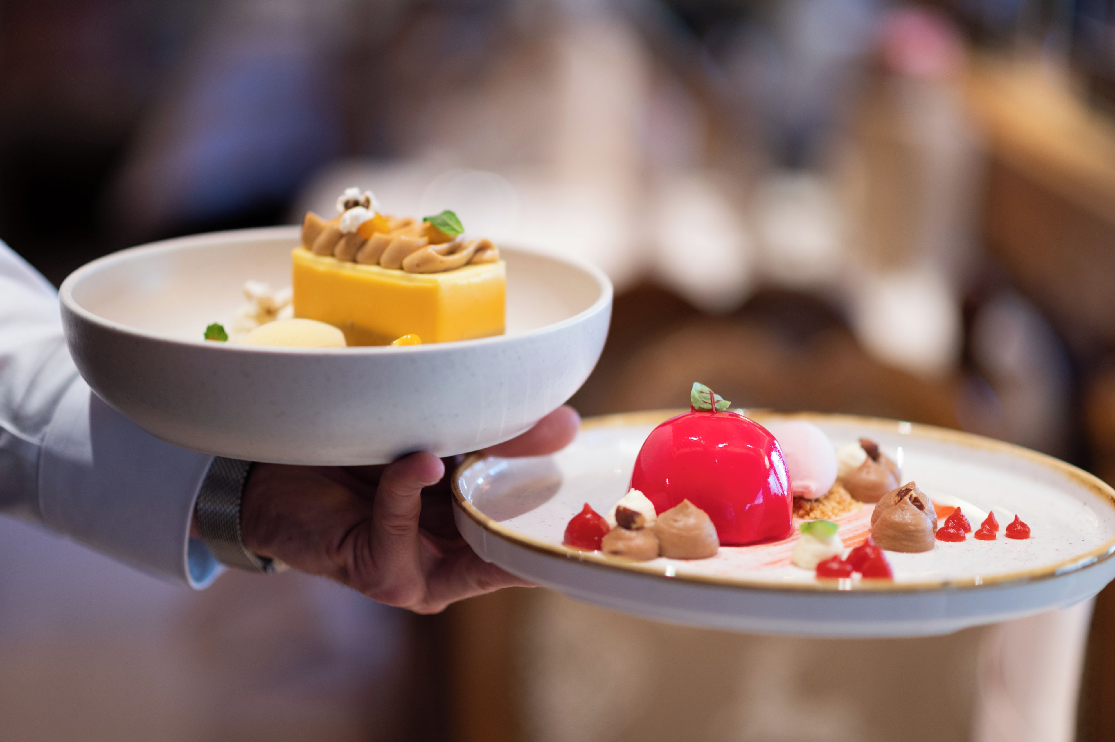 A person holding two plates with desserts.