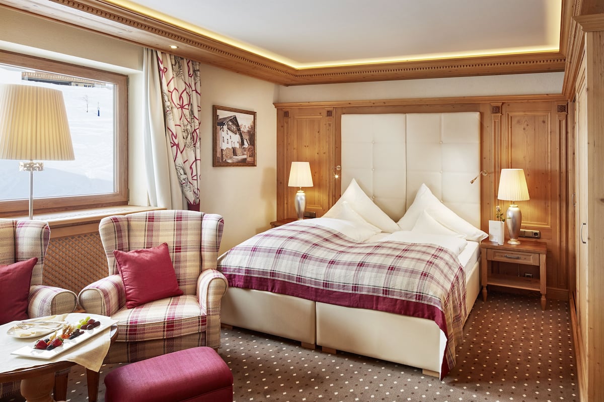 Une chambre d’hôtel avec un lit, une chaise, une table avec un plateau de nourriture et une fenêtre avec des rideaux.