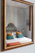Un dormitorio con cama, almohadas, cabecero y espejo.