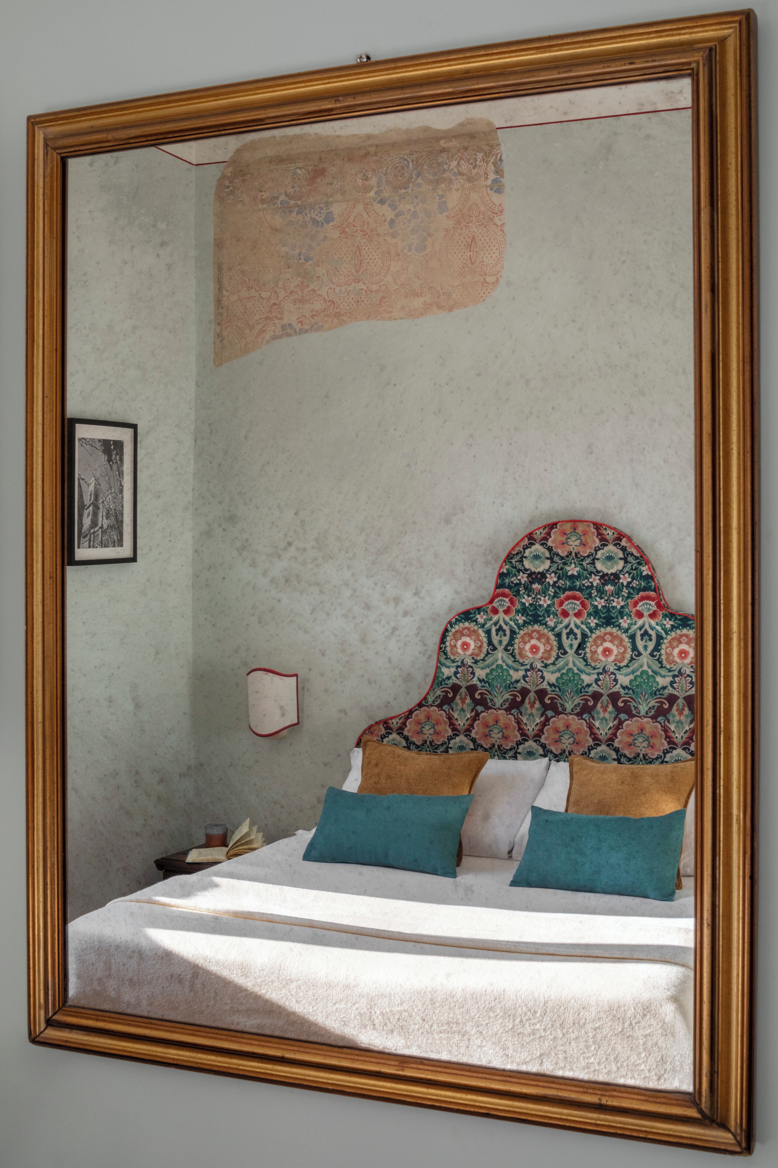 A bedroom with a bed, pillows, a nightstand, a framed picture, and a mirror.