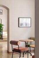 A modern interior with a round table and two chairs, a framed picture on the wall, and a staircase in the background.