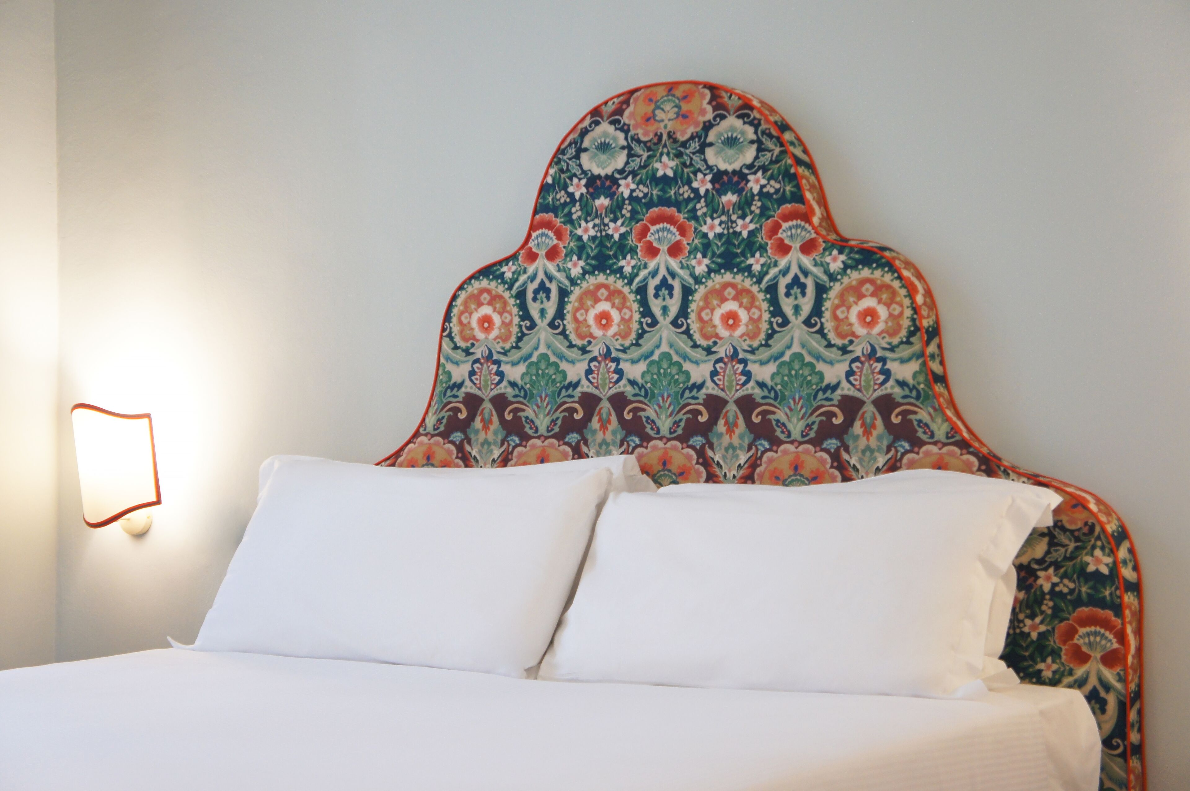 A bed with white linens and a headboard with a floral pattern.